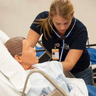Nursing student with stethoscope leaning over a model patient